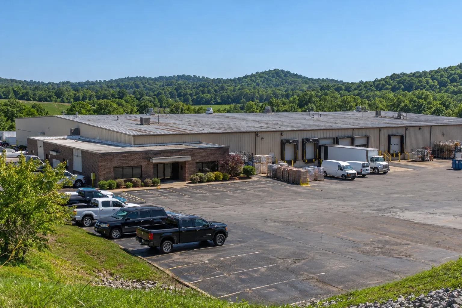 Low industrial building with a metal roof beside a parking lot and box trucks